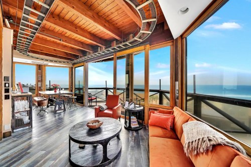 Modern living room with large windows, ocean view, wooden ceiling, and stylish furniture in a bright, airy space.