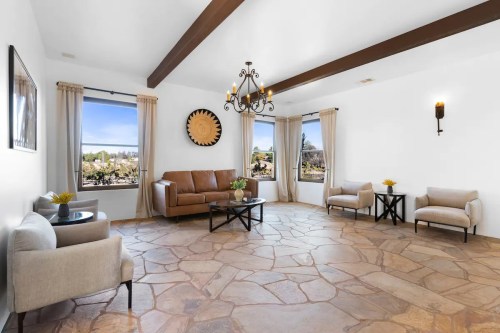Spacious living room with stone floor, brown leather sofa, two armchairs, and large windows with scenic views.