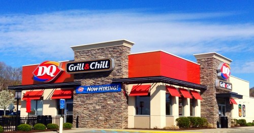 DQ Grill & Chill restaurant with a "Now Hiring" sign, featuring a stone facade and bright blue sky.