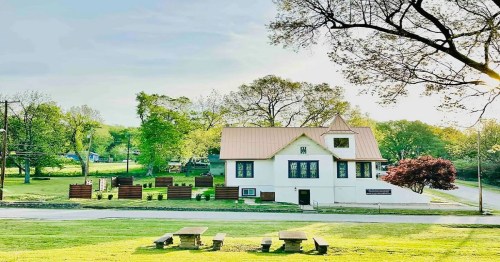 A charming white house with a copper roof, surrounded by greenery and trees, set in a peaceful landscape.
