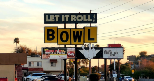 Sign for a bowling alley featuring the text "LET IT ROLL!" and "BOWL," with nearby restaurant and bar advertisements.