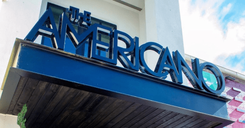 Sign for "The Americano" with bold letters against a blue background, set in a modern architectural style.