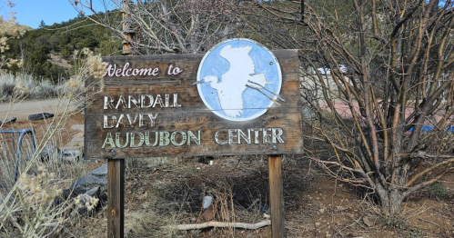 Wooden sign welcoming visitors to the Randall Davey Audubon Center, featuring a blue circle with a bird silhouette.
