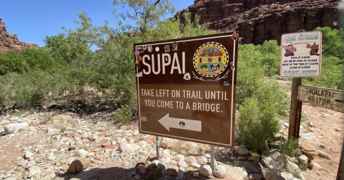 Signpost indicating "Supai" with directions to take a left until reaching a bridge, surrounded by rocky terrain.