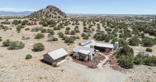 Aerial view of a desert landscape featuring a house, outbuilding, and a rocky hill in the background.