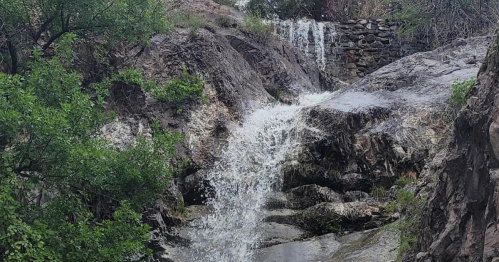A small waterfall cascading over rocky terrain, surrounded by green foliage and natural scenery.