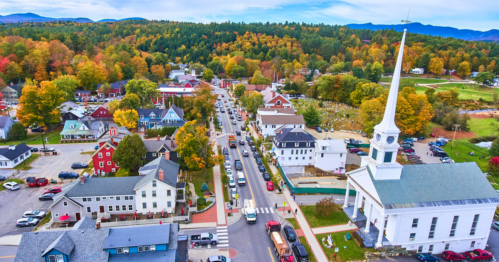 Aerial view of a charming town with colorful autumn trees, a church steeple, and bustling streets lined with cars.