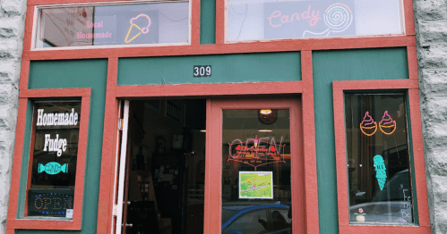 Colorful storefront with signs for ice cream, candy, and homemade fudge, featuring neon lights and an "Open" sign.