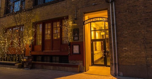 A warmly lit entrance to a brick building adorned with string lights, inviting and welcoming atmosphere.
