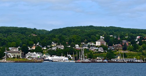 A scenic view of a waterfront town with lush green hills, boats docked, and charming houses along the shore.