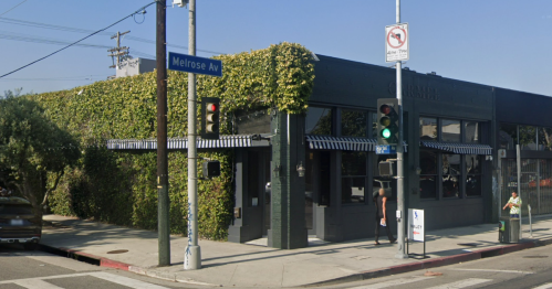 A street corner featuring a building covered in greenery, with traffic lights and a street sign for Melrose Ave.