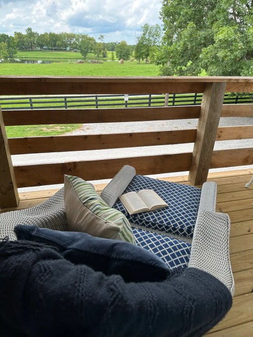 Cozy outdoor seating with a book on a cushion, overlooking a green landscape and wooden fence.