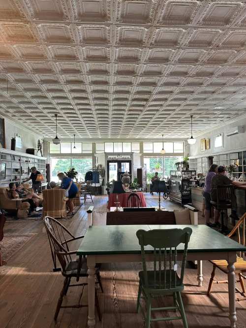 A cozy vintage shop with a patterned ceiling, showcasing furniture and decor, and people browsing inside.
