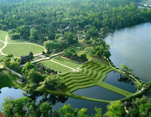 Aerial view of a lush green landscape with manicured lawns, ponds, and a winding path near a lake.