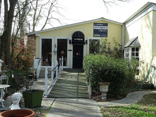 A charming antique shop with a welcoming entrance, surrounded by greenery and decorative items.