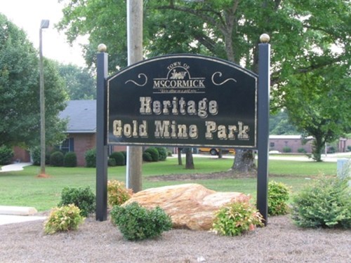 Sign for Heritage Gold Mine Park in McCormick, featuring decorative elements and surrounded by landscaped plants.