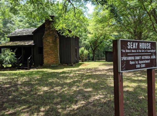 Historic Seay House surrounded by trees, with a sign indicating it's the oldest house in Spartanburg. Open by appointment.