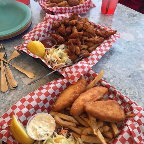 Three baskets of fried food on a table, featuring chicken tenders, fish, fries, coleslaw, and lemon wedges.