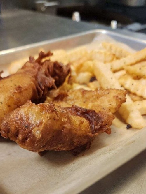 Two pieces of golden-brown fried fish served with a side of crispy French fries on a metal tray.