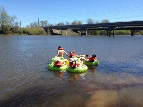 A group of people in colorful inner tubes floating on a calm river under a clear blue sky.