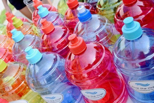 Colorful water bottles in various shades arranged neatly on a table, each with a label reading "Meet the River."