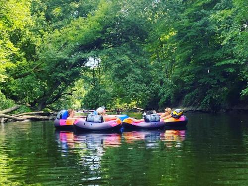 Two people relax on colorful inner tubes in a serene, tree-lined river.