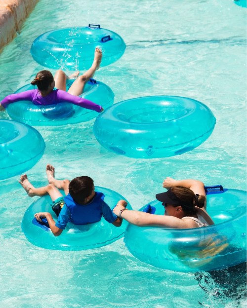 Two children and an adult float on blue inner tubes in a water park pool, enjoying a sunny day.