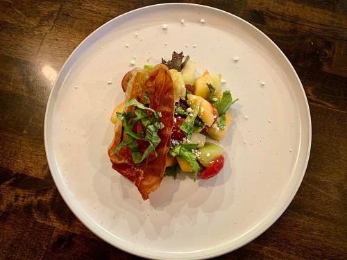 A plate of salad topped with crispy bacon, mixed greens, and colorful diced fruits, garnished with fresh herbs.