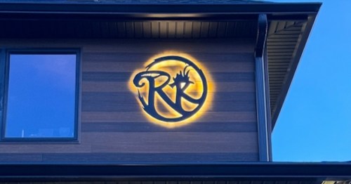 A house exterior featuring a large illuminated logo with the letters "RK" against a wooden panel background.