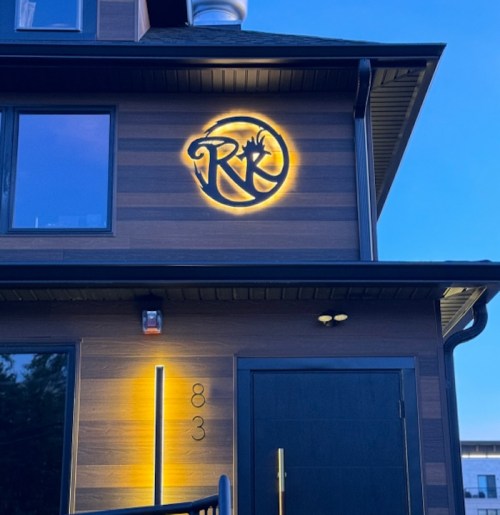 A modern building exterior featuring a lit logo and sleek design elements at dusk.