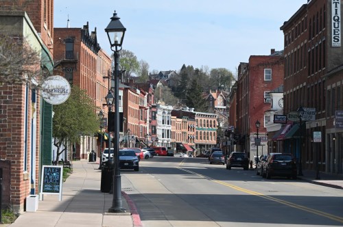 A quiet street lined with historic brick buildings, shops, and parked cars on a sunny day.