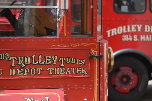 Red trolley with "Trolley Tours Depot Theater" signage, parked alongside another red trolley.