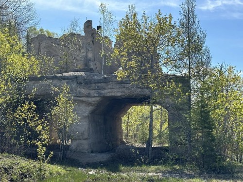 Ruins of a stone structure surrounded by greenery and trees under a clear blue sky.