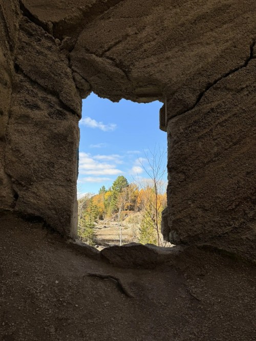 View through a stone window frame, showcasing a blue sky and autumn trees in the distance.