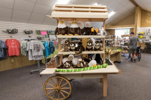 A display cart filled with various plush animal toys in a gift shop, with shelves stacked high and a customer browsing nearby.
