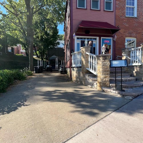 A quaint building with a red awning and "OPEN" sign, surrounded by trees and a paved walkway.