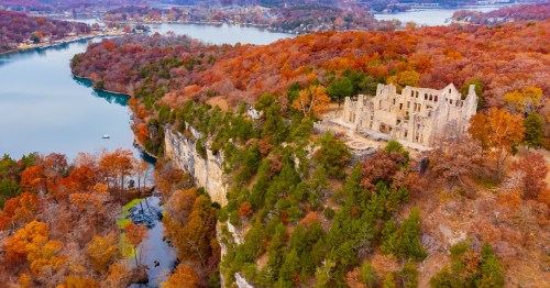 Aerial view of a ruined building surrounded by vibrant autumn foliage and a winding river below.