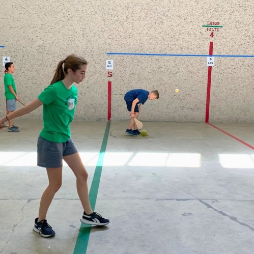 A girl in a green shirt plays a ball game indoors, while two boys participate in the background.