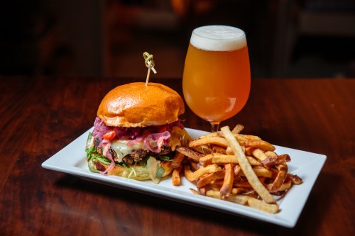 A gourmet burger with toppings, served with fries and a glass of beer on a wooden table.