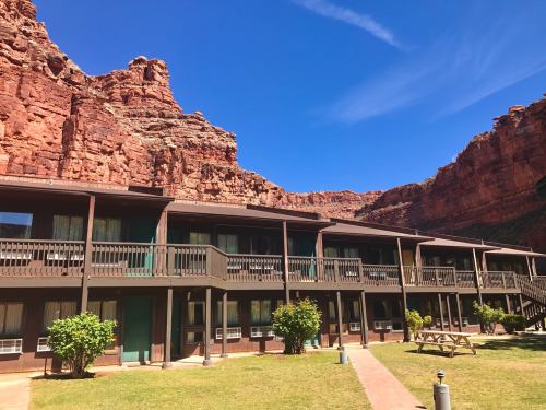 A two-story lodge surrounded by red rock formations under a clear blue sky, with green shrubs in the foreground.