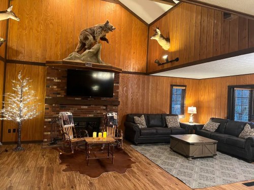 Cozy living room with wooden walls, a mounted bear, a TV, and comfortable seating around a coffee table.