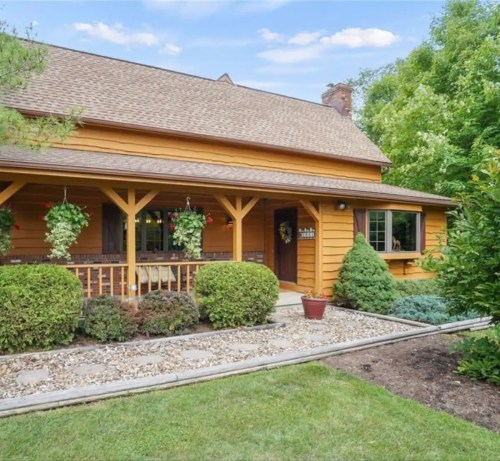 A charming yellow wooden house with a porch, surrounded by greenery and well-maintained landscaping.