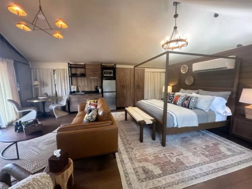 Cozy hotel room featuring a king bed, seating area, kitchenette, and warm lighting in a modern design.