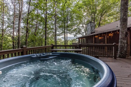 A hot tub on a wooden deck surrounded by lush trees, with a view of distant mountains in the background.