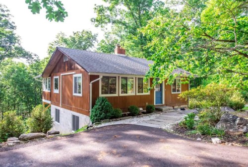 A modern wooden house surrounded by trees, featuring a stone pathway and a blue front door.
