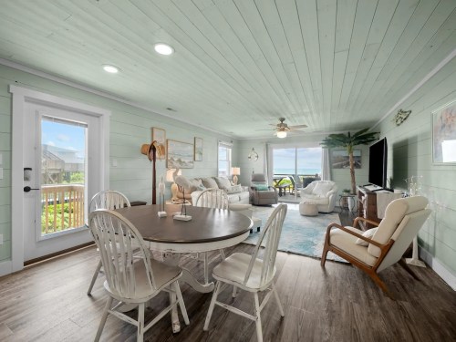 Bright coastal living room with light green walls, a round dining table, and large windows showcasing a scenic view.