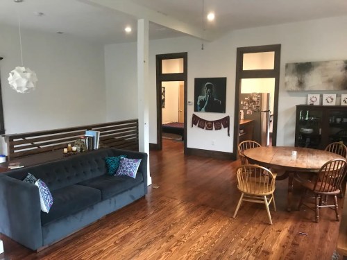 A cozy living space featuring a gray couch, wooden dining table, and open layout with warm wooden floors.