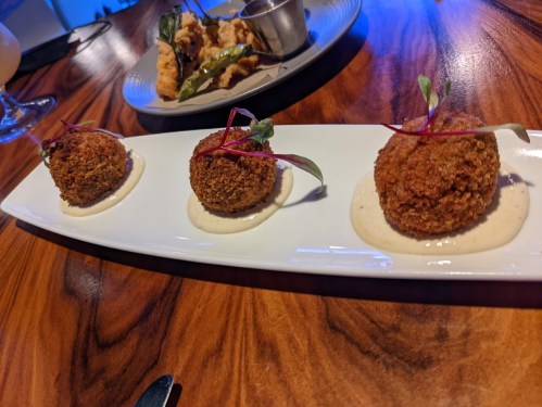 Three crispy croquettes on a white plate, garnished with microgreens and served with a creamy sauce.