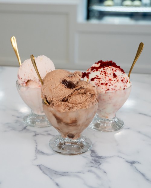Three ice cream sundaes in glass bowls: chocolate, red velvet, and strawberry, each with a gold spoon.