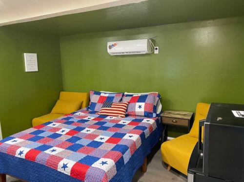 Cozy room with a green wall, a bed with a colorful quilt, two yellow chairs, and a small table.